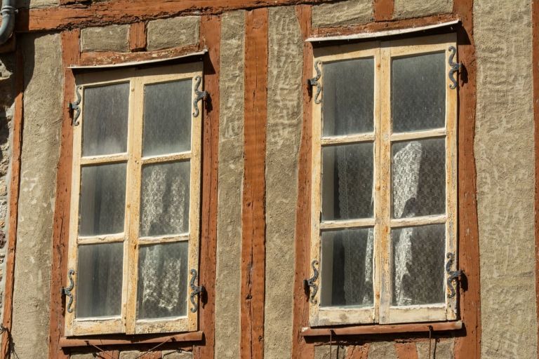 Zwei alte Holzfenster mit Sprossen in einer verputzten Fachwerkwand