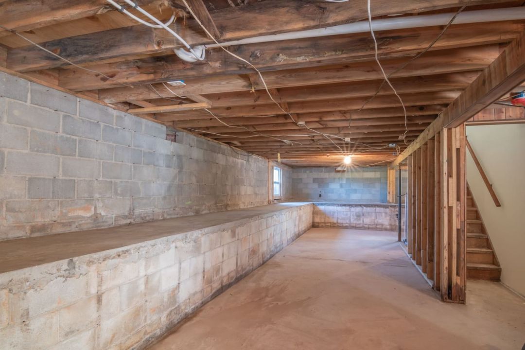 Unverputzter Keller mit Betonsteinwand, offener Balkendecke und Treppe