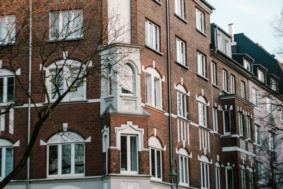Backsteinfassade eines älteren Mehrfamilienhauses mit hellen Fensterbänken an einer Wohnstraße