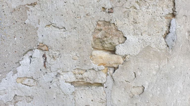 Nahaufnahme einer Wand mit abblätterndem Putz und darunterliegendem Stein